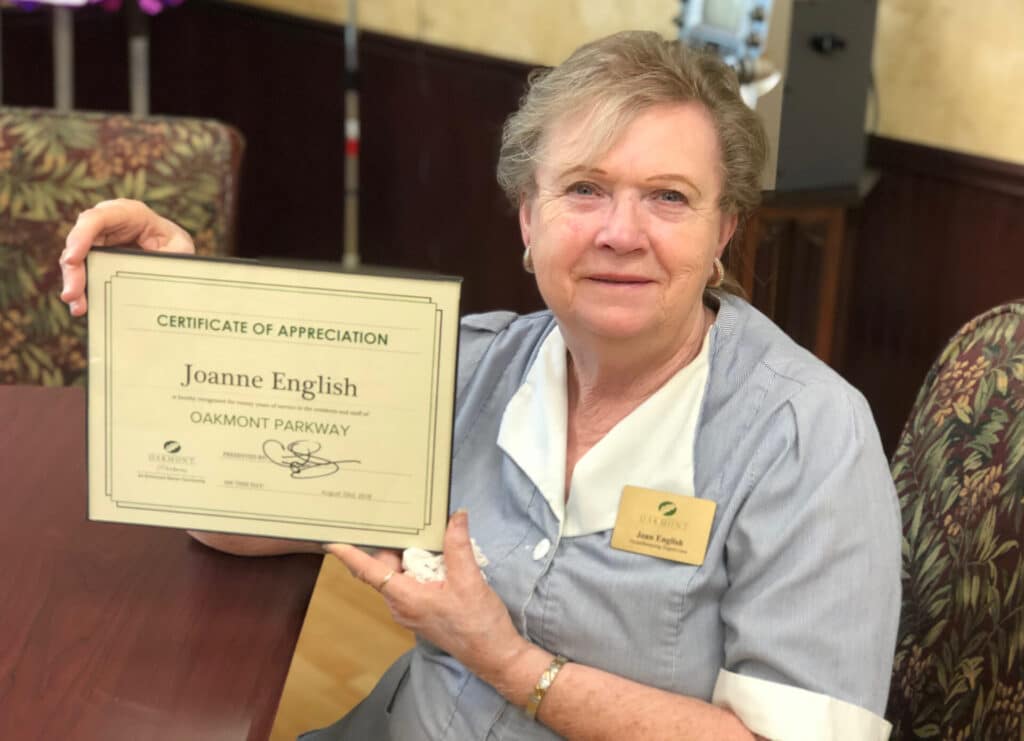 Elderly woman smiling holding framed certificate
